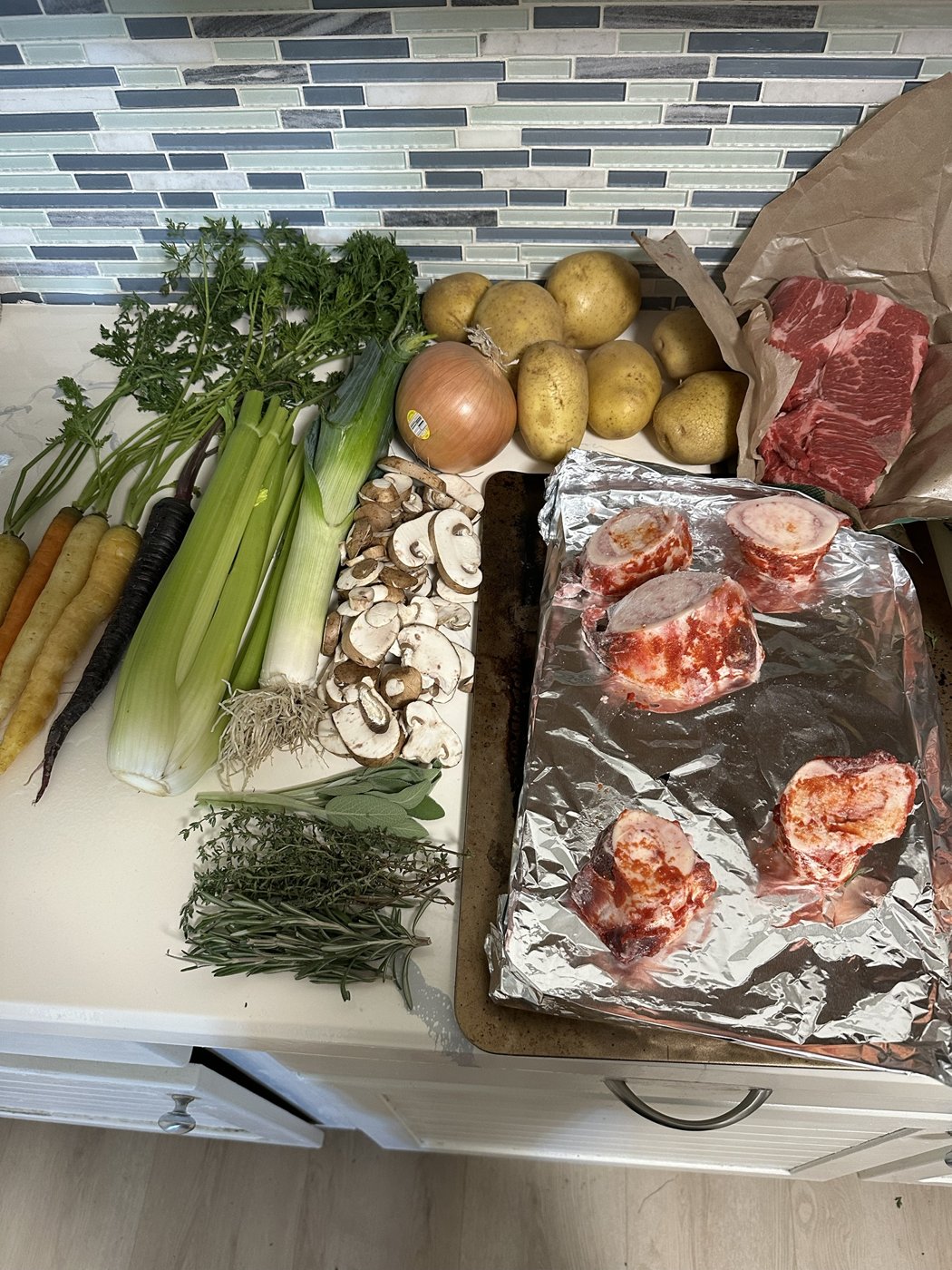 Fresh vegetables, herbs, potatoes and beef prepped on a kitchen counter